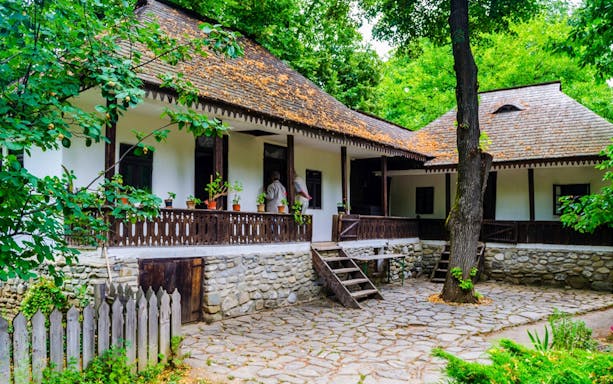 Traditional Romanian house at Bucharest Village Museum, surrounded by lush greenery.