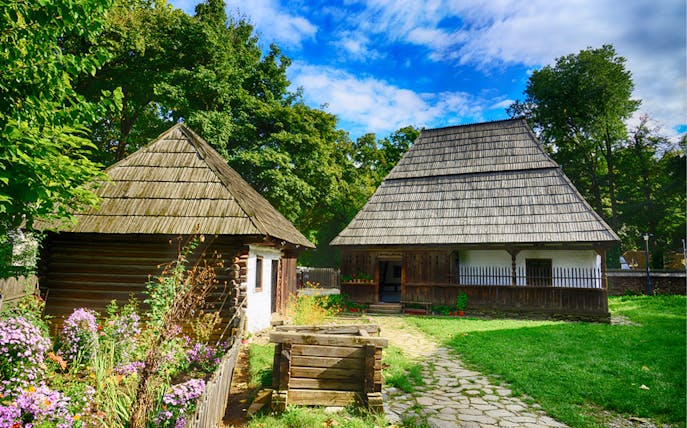 Traditional wooden houses at Village Museum, Bucharest, surrounded by lush greenery and flowers.