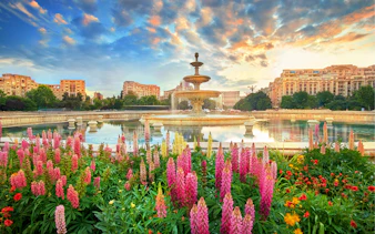 Fountain in Bucharest surrounded by colorful flowers at sunset, part of a private sightseeing tour.