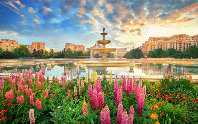 Fountain in Bucharest surrounded by colorful flowers at sunset, part of a private sightseeing tour.