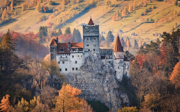 Bran Castle in autumn, surrounded by colorful trees, part of Dracula's life journey tour in Romania.