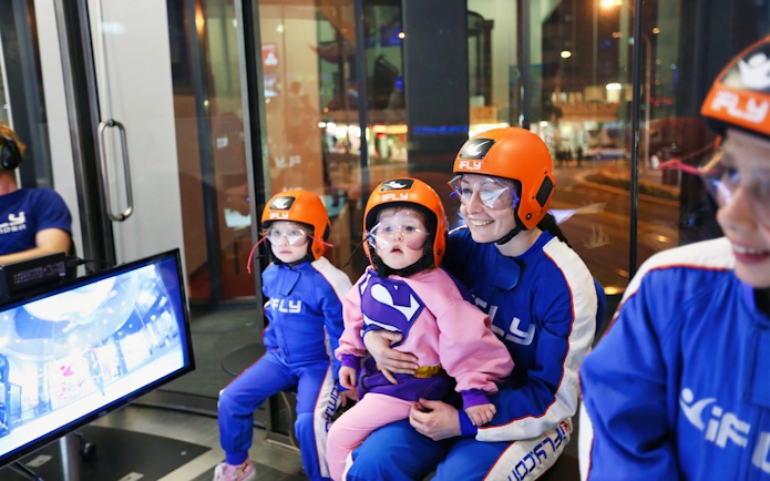 Family preparing for iFLY indoor skydiving experience, wearing flight suits and helmets.
