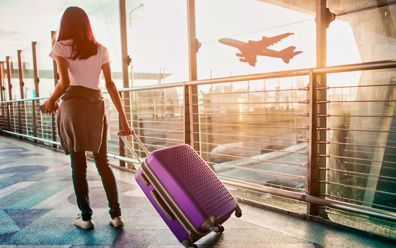 Traveler with suitcase at Cairo airport terminal, airplane silhouette in background.
