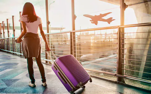 Traveler with suitcase at Cairo airport terminal, airplane silhouette in background.