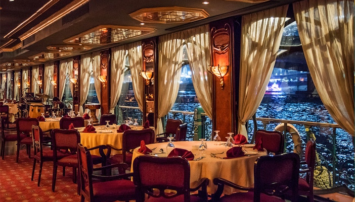 Elegant dining setup on the Nile Maxim cruise with river view through large windows.