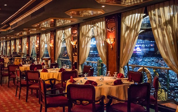 Elegant dining setup on the Nile Maxim cruise with river view through large windows.