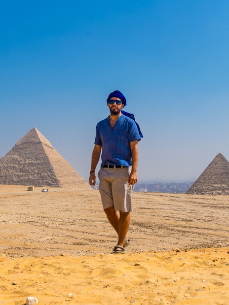 Man walking near the Pyramids of Giza, Egypt, under a clear blue sky.