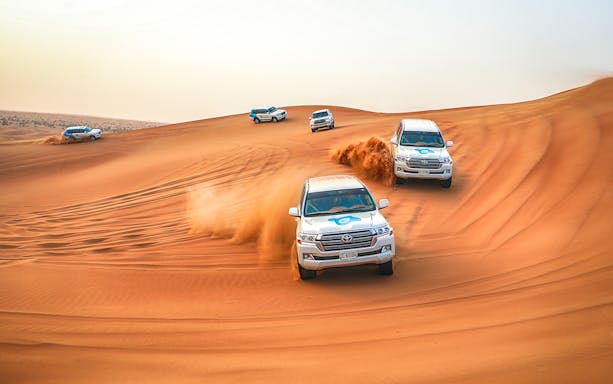 SUVs driving through desert dunes during a quad bike and dune bashing adventure.