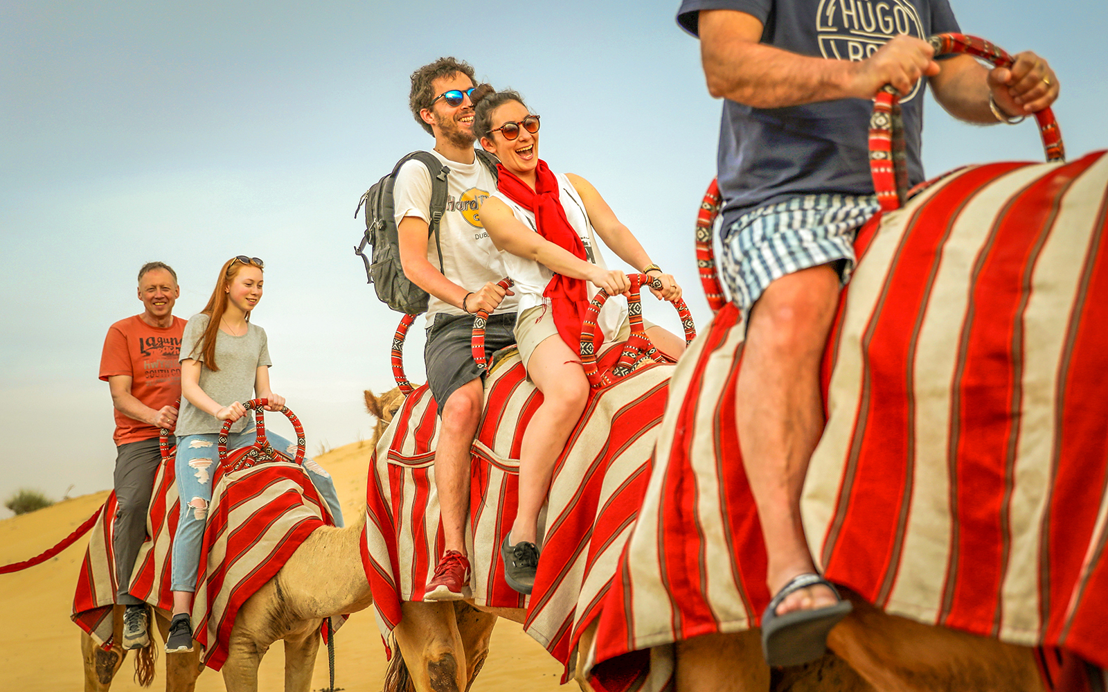 Tourists enjoying a camel ride in the desert during a quad bike and dune bashing adventure.