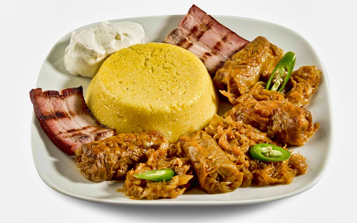 Traditional Romanian meal with polenta, cabbage rolls, bacon, and sour cream.