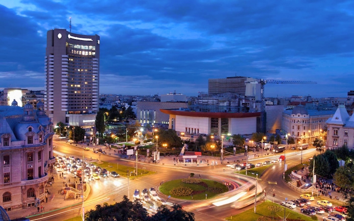 Cityscape of Bucharest at night with illuminated buildings and busy roundabout.