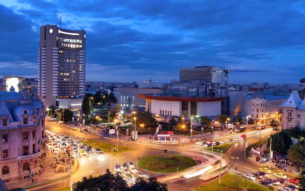 Cityscape of Bucharest at night with illuminated buildings and busy roundabout.
