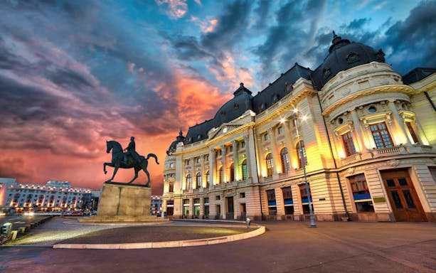 Equestrian statue and illuminated historic building at sunset on After Dark City Tour.