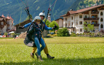 Tandem paragliding landing in Tirol with scenic alpine village backdrop.