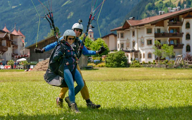 Tandem paragliding landing in Tirol with scenic alpine village backdrop.