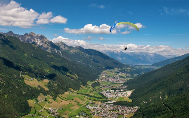 Tandem paragliding over scenic valley and mountains in Tirol, Austria.