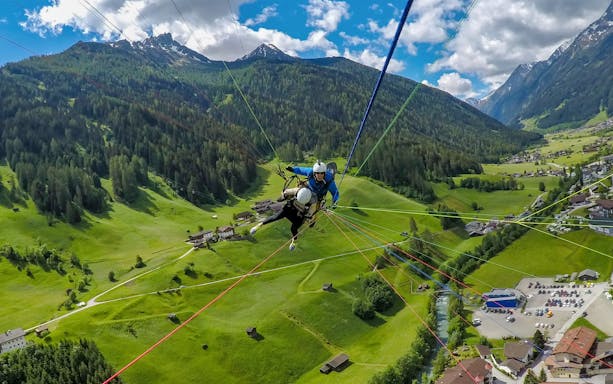 Tandem paragliding over green valleys and mountains in Tirol, Austria.