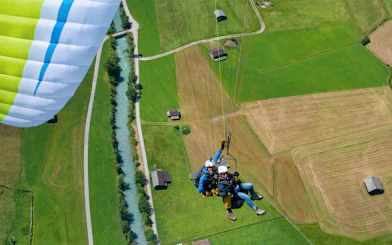 Tandem paragliding over green fields and river in Tirol, Austria.