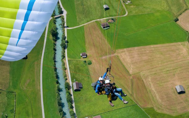 Tandem paragliding over green fields and river in Tirol, Austria.