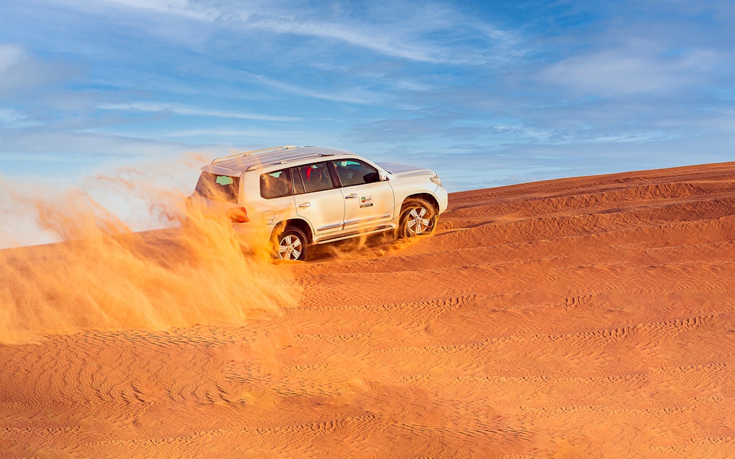 SUV driving through Dubai desert dunes on a safari adventure.
