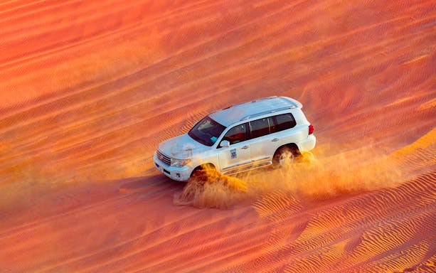 SUV driving through desert dunes during a Dubai safari tour.