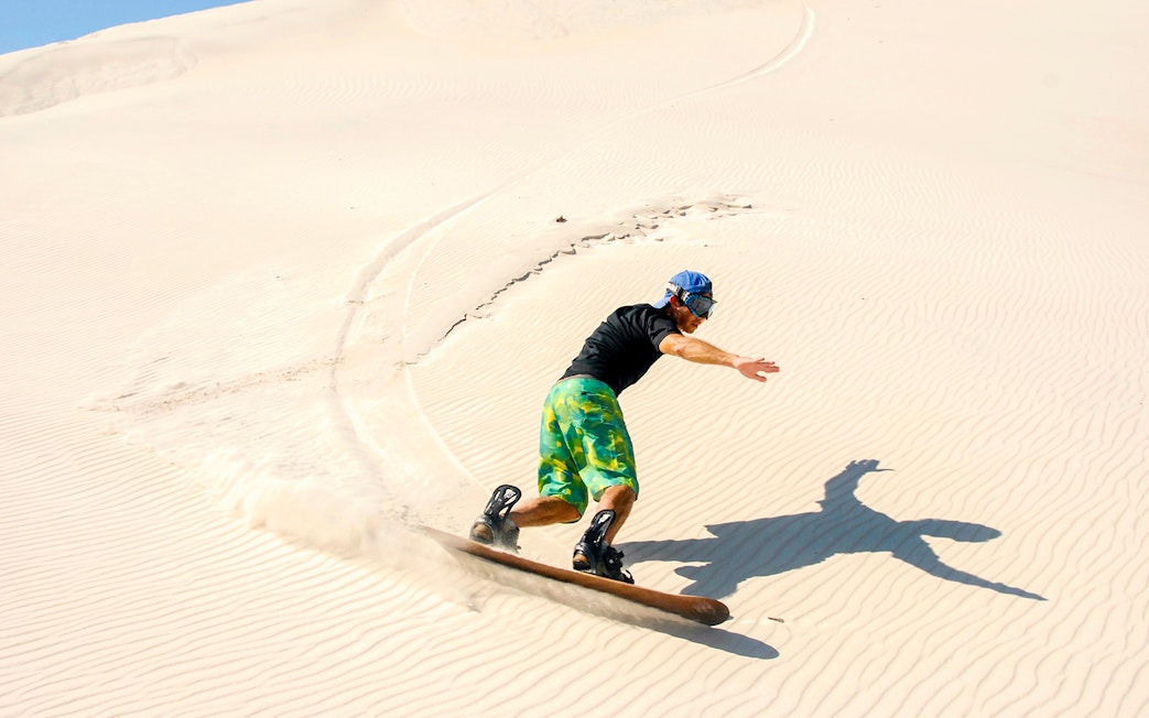 Person sandboarding on Dubai desert dunes.