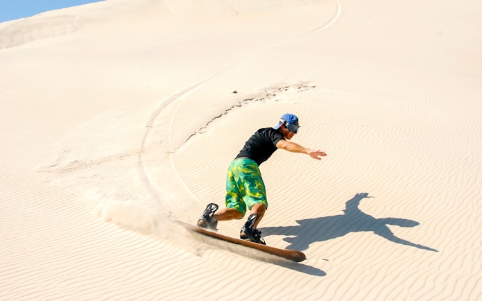 Person sandboarding on Dubai desert dunes.