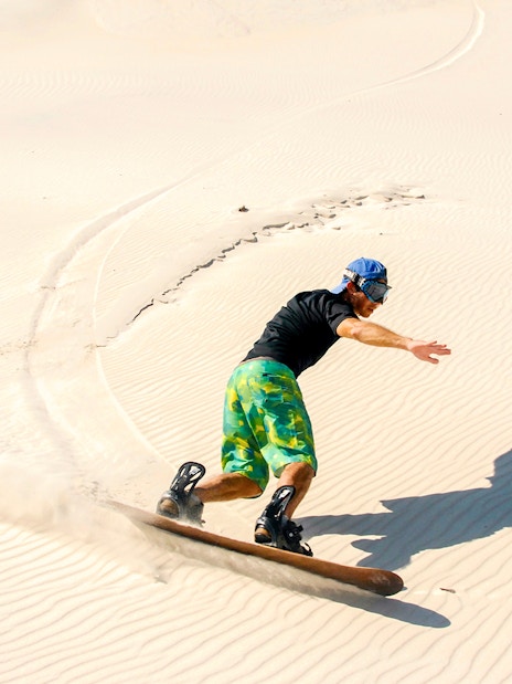 Person sandboarding on Dubai desert dunes.