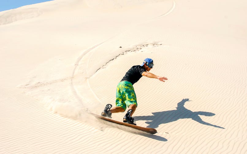 Person sandboarding on Dubai desert dunes.