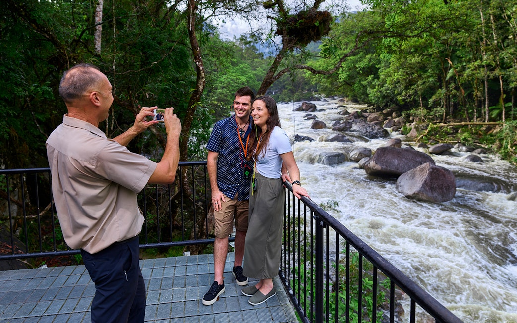 Couple posing for a photo at Mossman Gorge lookout, surrounded by lush rainforest and river.