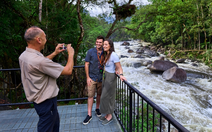 Couple posing for a photo at Mossman Gorge lookout, surrounded by lush rainforest and river.