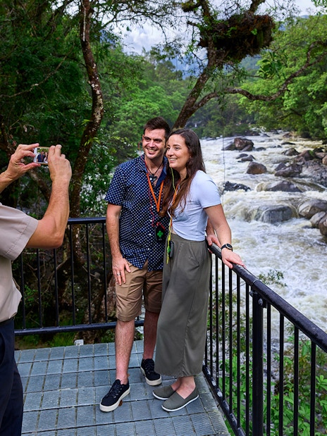 Couple posing for a photo at Mossman Gorge lookout, surrounded by lush rainforest and river.