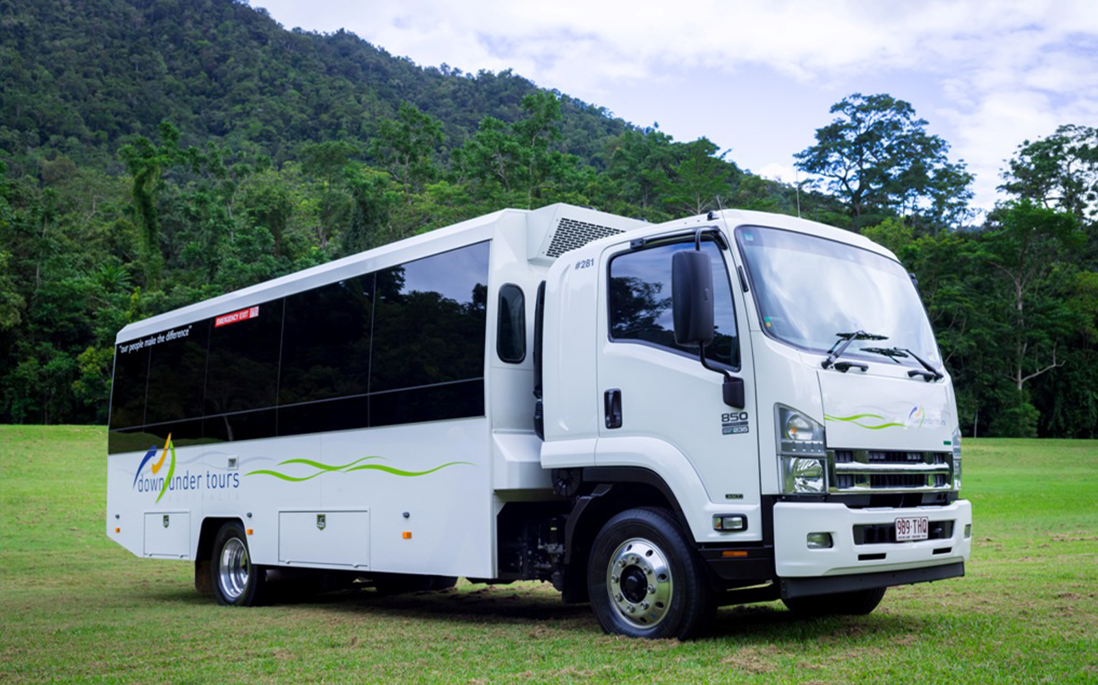 Tour bus for Cape Tribulation, Daintree & Mossman Gorge tour parked in lush green landscape.