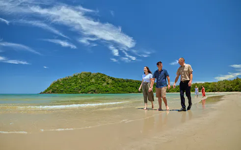 Tour group walking along Cape Tribulation beach with lush greenery in the background.