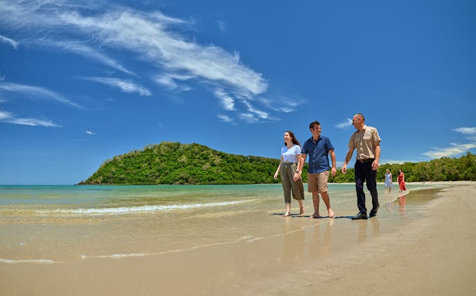 Tour group walking along Cape Tribulation beach with lush greenery in the background.