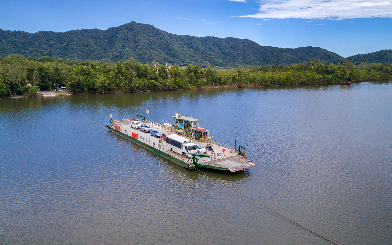 Ferry crossing Daintree River with vehicles, surrounded by lush rainforest and mountains in Cape Tribulation.