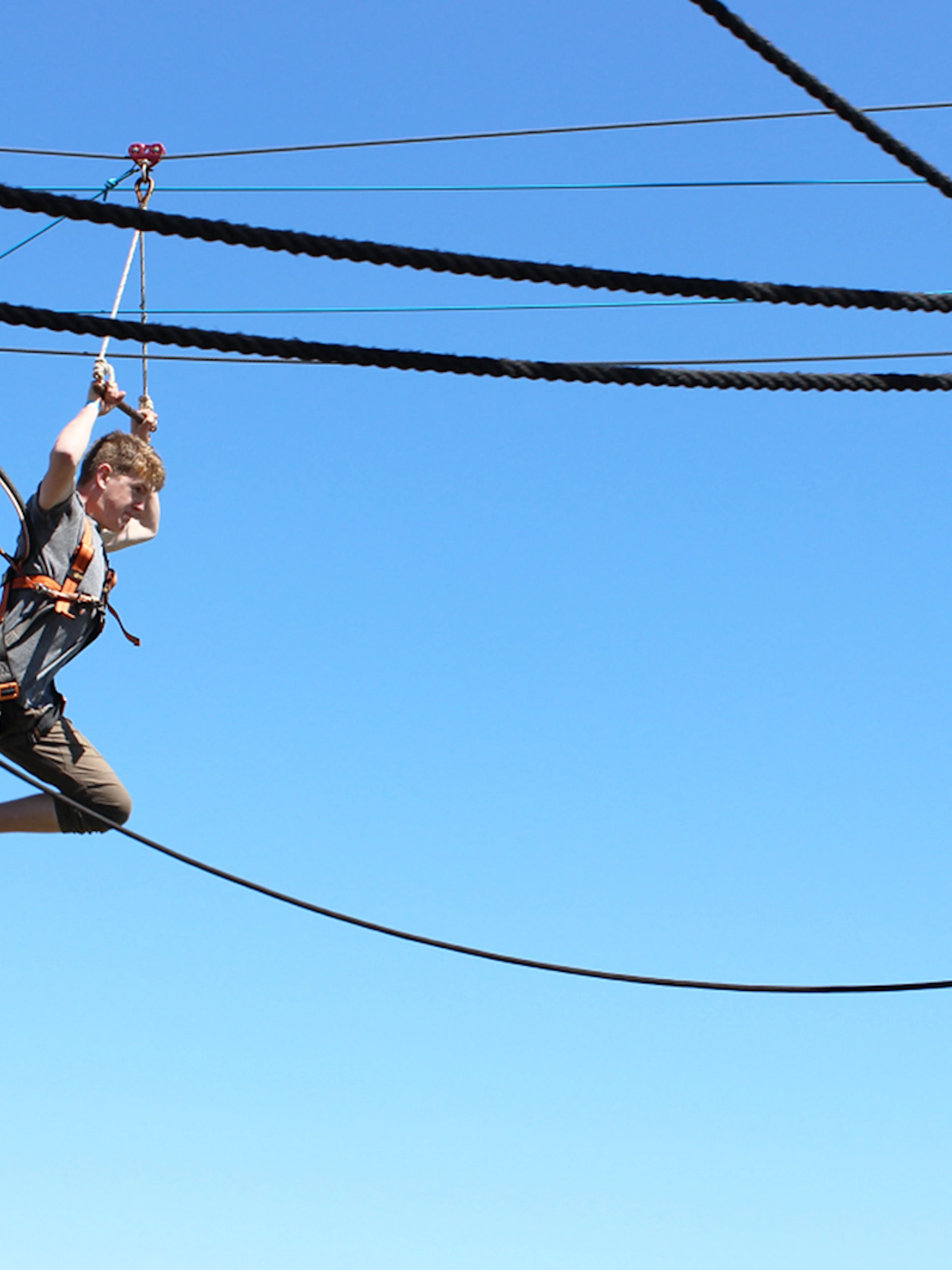 Person ziplining at West Beach Adventure against a clear blue sky.