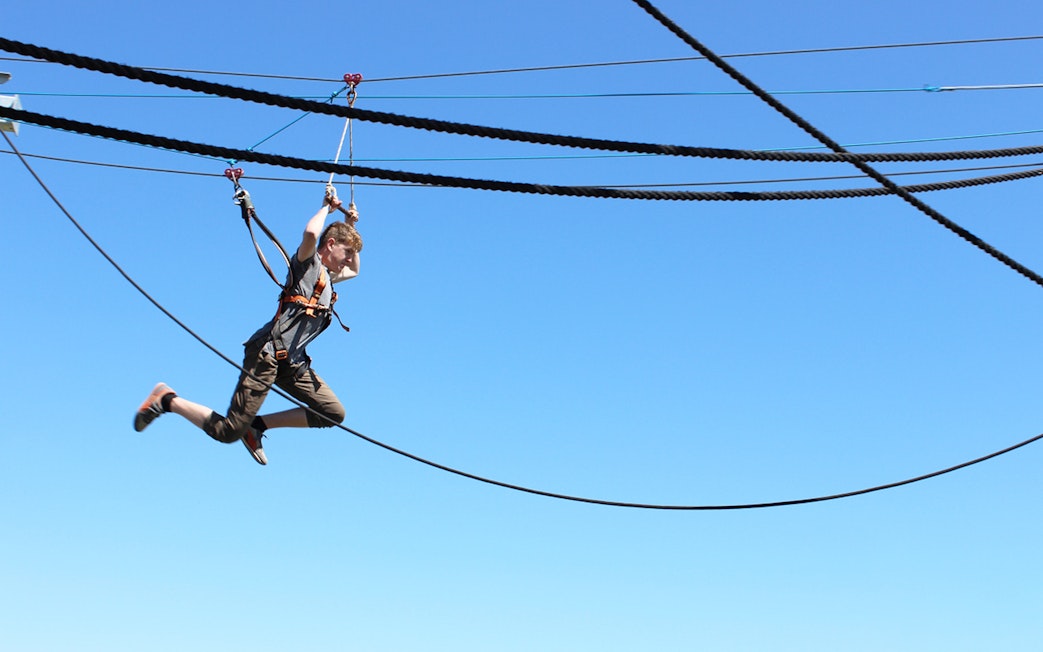 Person ziplining at West Beach Adventure against a clear blue sky.
