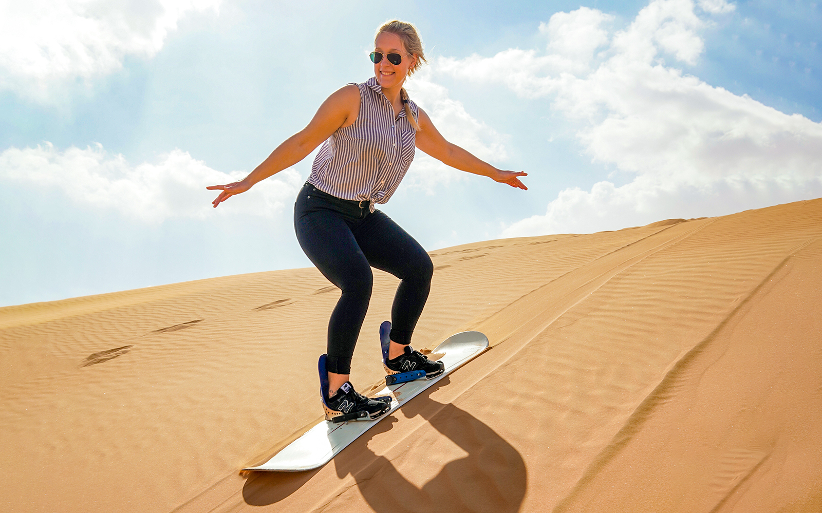 Person sandboarding down a desert dune under a clear sky.