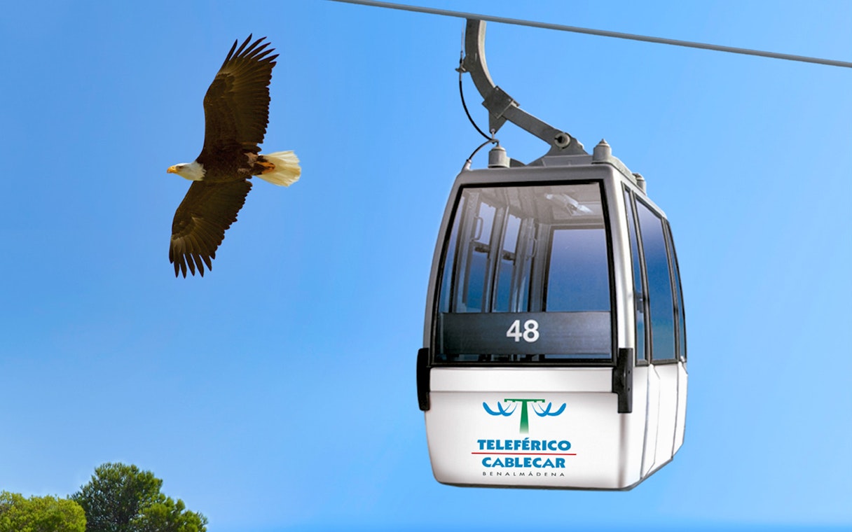 Benalmadena cable car with bird flying nearby against blue sky.