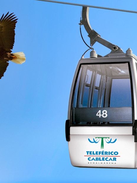 Benalmadena cable car with bird flying nearby against blue sky.