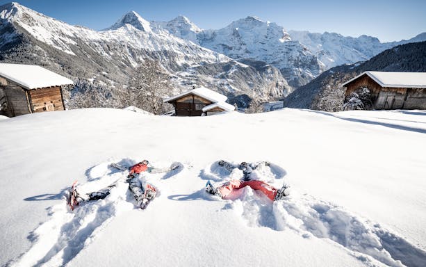 Snowshoers making snow angels near wooden cabins with Swiss Alps backdrop, Isenfluh tour.