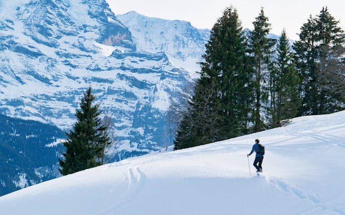 Snowshoer ascending snowy slope towards Lobhornhütte, Swiss Alps backdrop.