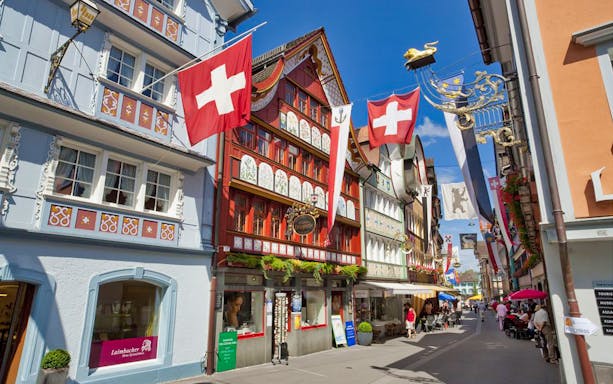 Colorful traditional buildings and Swiss flags in Appenzell, Switzerland, on a sunny day.