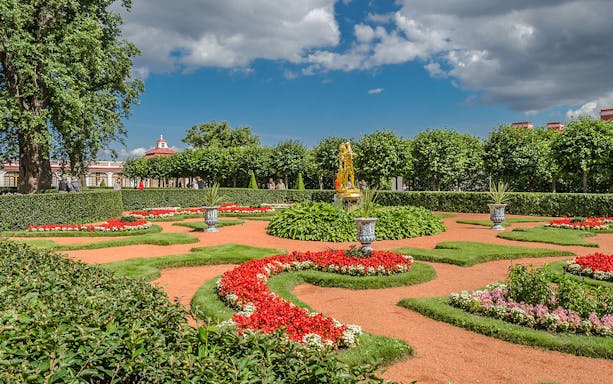 Peterhof Grand Palace gardens with vibrant flower beds and a golden statue.