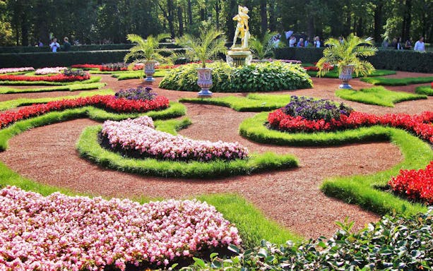 Peterhof Grand Palace gardens with vibrant flower beds and a central statue.