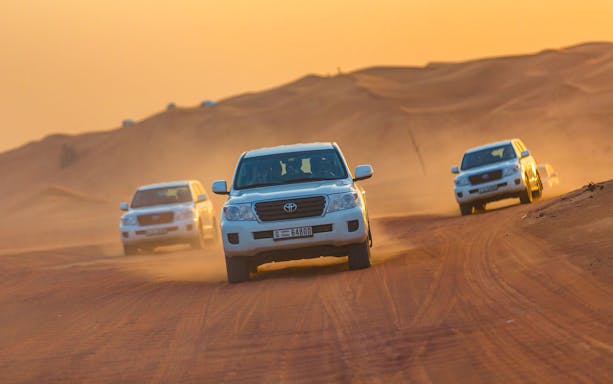 SUVs driving through desert dunes during a sunset safari in Dubai.