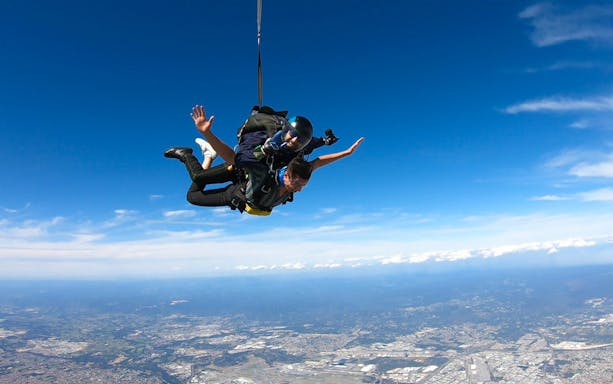 Tandem skydive over Perth city from 14,000 feet, showcasing expansive cityscape and blue sky.
