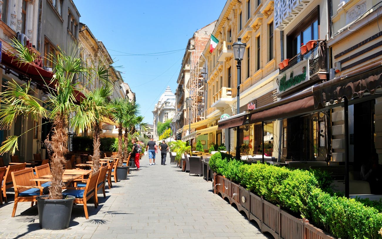 Street cafes and historic buildings in Old Town Bucharest during a walking food tour.