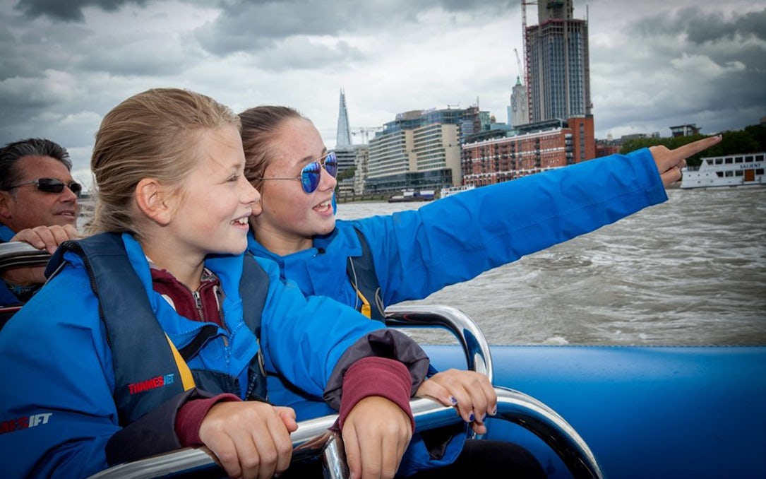 People enjoying a high-speed boat ride on the Thames River with London skyline in view.